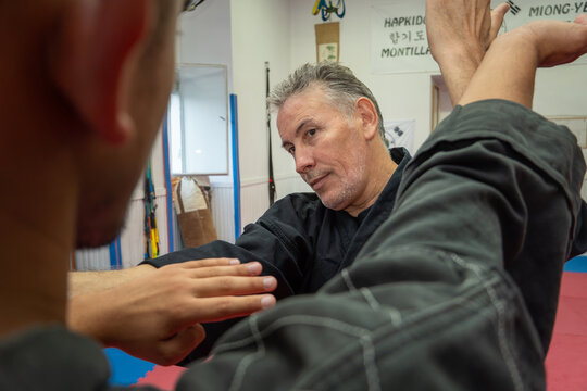Hapkido master demonstrating a defensive arm lock technique on a male student during martial arts training in a dojang