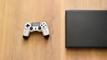 Wireless gamepad and closed gaming laptop lying on wooden table top view © Yanina