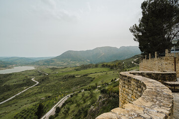 Stone castle wall overlooking a green valley, reservoir, and winding road © Puripat