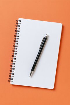 Blank spiral notebook with black pen on a bright orange background, minimalist stationery mockup with clean copy space