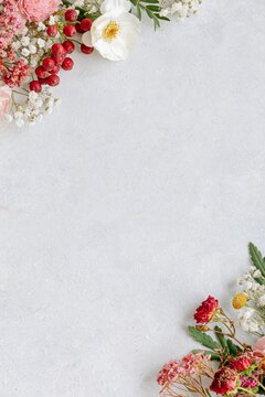 Delicate floral frame with pink, white and red flowers arranged around a light textured background with generous copy space