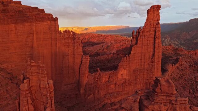 Warm evening light bathes towering sandstone spires and rugged desert canyons during a sweeping aerial flight near Moab Utah