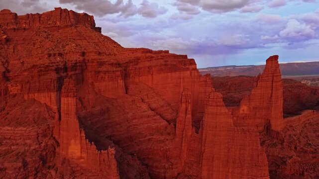 Warm evening light bathes towering sandstone spires and rugged desert canyons during a sweeping aerial flight near Moab Utah