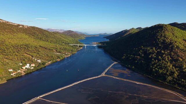 Aerial view of the bridge over the bay in Ston, Croatia, with salt pans and green hills on a sunny day