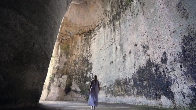 Young Woman walks in the Ancient Cave in Syracuse, Sicily, Italy. Ear of Dionysius, giant Cave with exceptional Acoustic