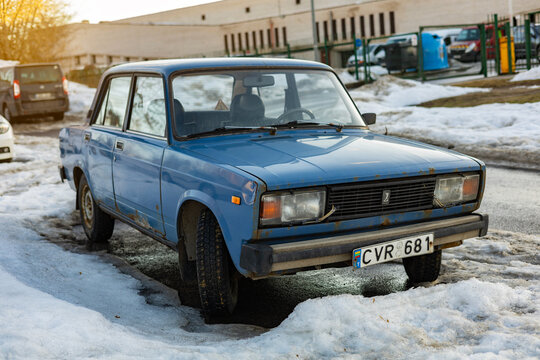 Vilnius, Lithuania - March 2 2026: Front view of classic blue Lada 2105 Soviet sedan parked on snowy winter street. Rust details on vintage body, frozen slush and wet asphalt after thaw.