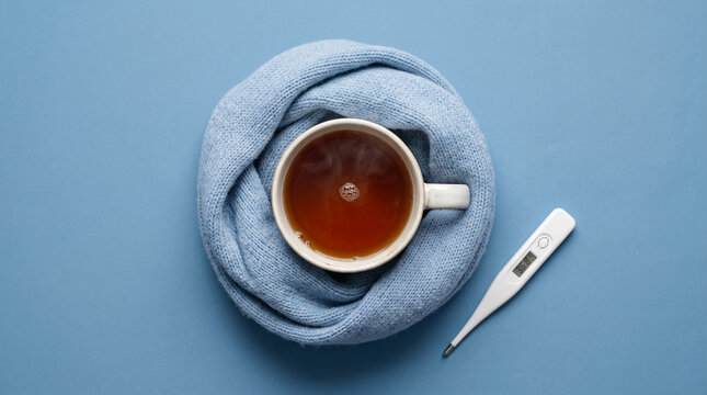 Hot tea and thermometer on blue background, cozy and illness concept