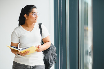 Indian student with backpack reading book near window