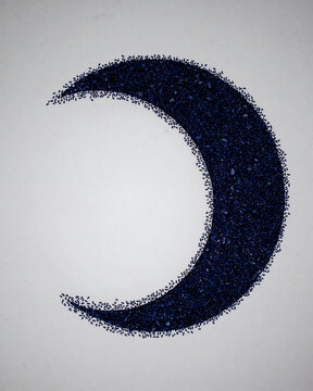 A crescent moon shape made of dark blue crushed stone or gravel particles on a plain white background, showing a grainy, and textured surface