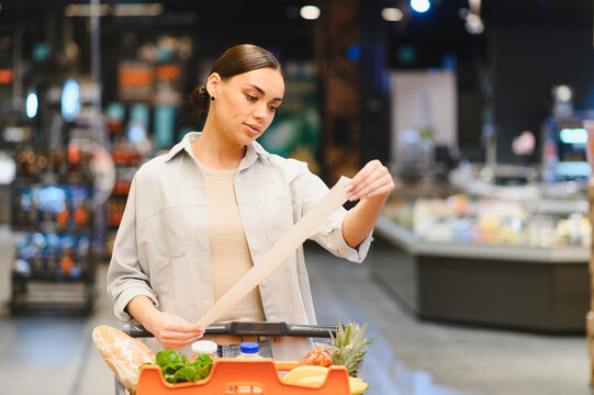 Woman checking long grocery receipt comparing prices in supermarket