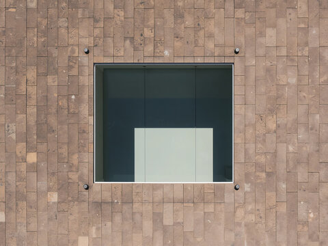 A square window with dark glass set into a textured brown stone tile wall with visible metal mounting bolts at each corner of the window frame