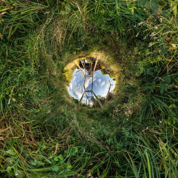 creative tiny planet photo of a rural landscape with dirt road, green fields, and cloudy sky forming a circular world.
