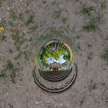 creative tiny planet photo of a rural landscape with dirt road, green fields, and cloudy sky forming a circular world.