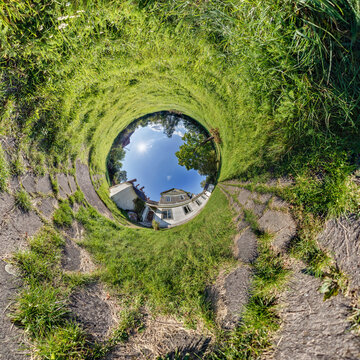 creative tiny planet photo of a rural landscape with dirt road, green fields, and cloudy sky forming a circular world.