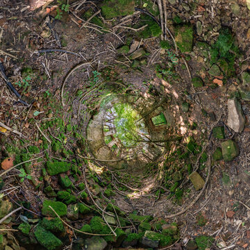 creative tiny planet photo of a rural landscape with dirt road, green fields, and cloudy sky forming a circular world.