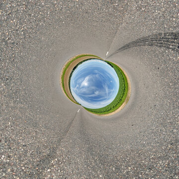 creative tiny planet photo of a rural landscape with dirt road, green fields, and cloudy sky forming a circular world.