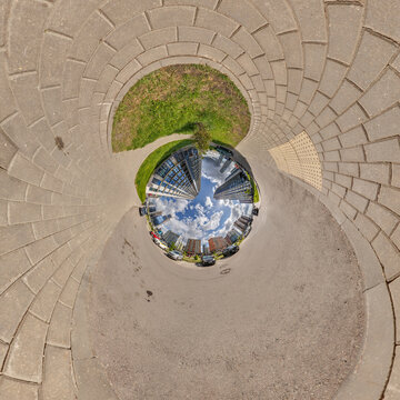 creative tiny planet photo of a rural landscape with dirt road, green fields, and cloudy sky forming a circular world.