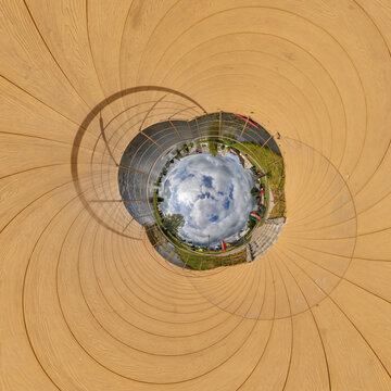 creative tiny planet photo of a rural landscape with dirt road, green fields, and cloudy sky forming a circular world.