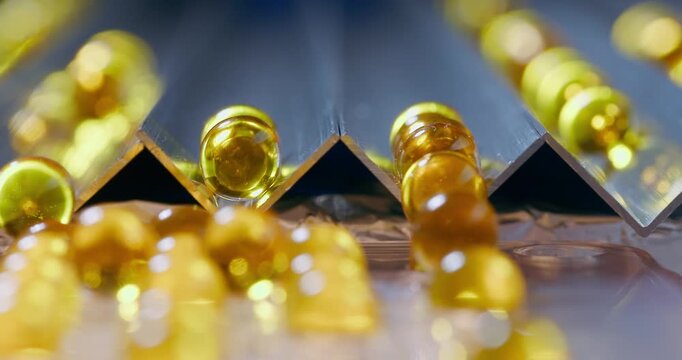 Slow motion rolling golden capsules down metal v groove channels on glossy surface in studio.