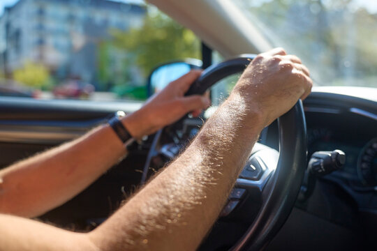 Driver holds steering wheel with both hands inside car on sunny city street