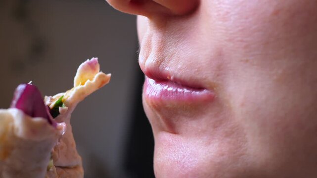 Person bites wrap near mouth, holding stuffed flatbread close while chewing. Close up food moment emphasizes lips, skin texture, and tender movement with quiet, satisfied mood in warm light.