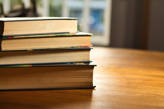 Pila de libros antiguos sobre mesa de madera con luz natural y espacio para texto
