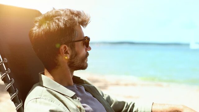 A man is sitting in a beach chair, looking out at the water