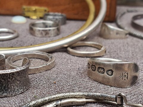 Close-up macro photograph of sterling silver rings displaying British hallmark stamps, arranged on a grey felt-lined surface. The image prominently features a vintage silver band in sharp focus