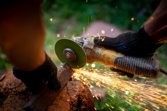 Man in protective gloves cutting metal with an angle grinder outdoors, bright sparks flying. Concept of manual labour, home workshop, DIY metalwork and work safety.