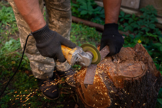 Man in protective gloves cutting metal with an angle grinder outdoors, bright sparks flying. Concept of manual labour, home workshop, DIY metalwork and work safety.