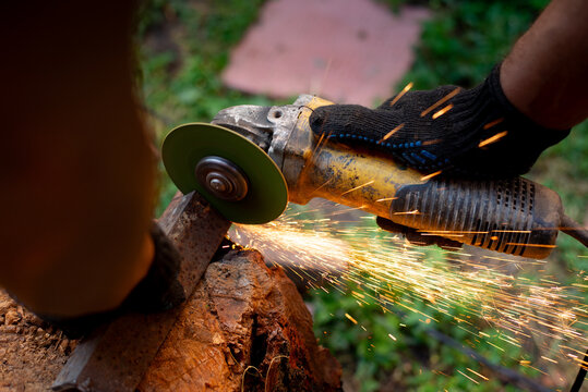 Man in protective gloves cutting metal with an angle grinder outdoors, bright sparks flying. Concept of manual labour, home workshop, DIY metalwork and work safety.