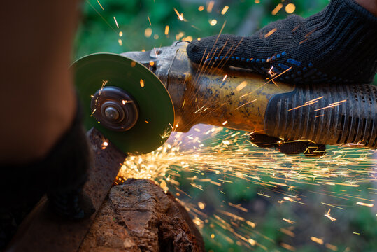 Man in protective gloves cutting metal with an angle grinder outdoors, bright sparks flying. Concept of manual labour, home workshop, DIY metalwork and work safety.
