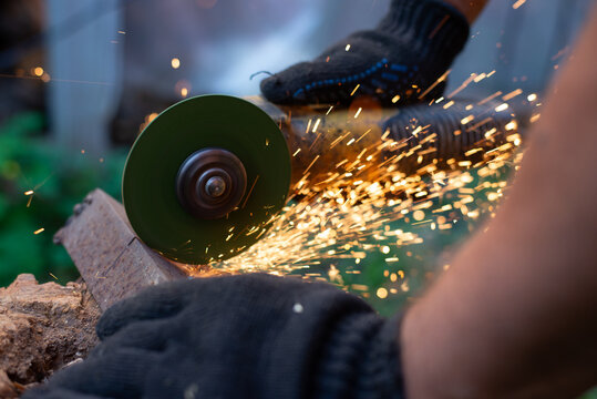 Man in protective gloves cutting metal with an angle grinder outdoors, bright sparks flying. Concept of manual labour, home workshop, DIY metalwork and work safety.