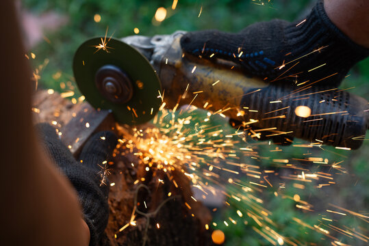 Man in protective gloves cutting metal with an angle grinder outdoors. Motion blur bright sparks flying. Concept of manual labour, home workshop, DIY metalwork and work safety.