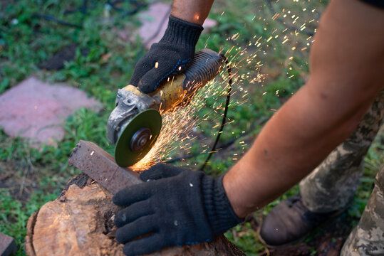 Man in protective gloves cutting metal with an angle grinder outdoors, bright sparks flying. Concept of manual labour, home workshop, DIY metalwork and work safety.
