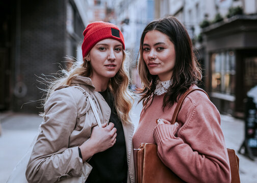 Two young women, likely white, posing on a city street in stylish casual clothes