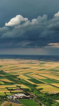 Aerial view of agricultural farmland under dramatic dark storm clouds. Rural landscape with village and fields. Vertical video 4k