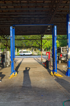 Open-air auto Bob Lee's Tire Company repair garage with multiple tire machines, blue hydraulic car lifts and service bays under a large metal canopy, showing tools, buckets and equipment arranged for 