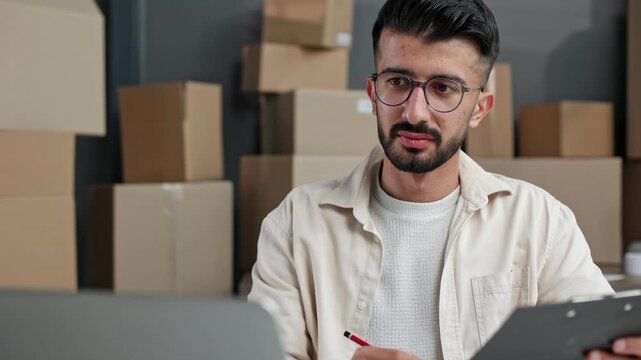 Man with glasses reviews files near stacked boxes