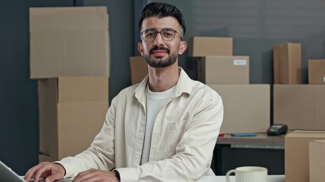 Man with glasses types on laptop in shipping warehouse