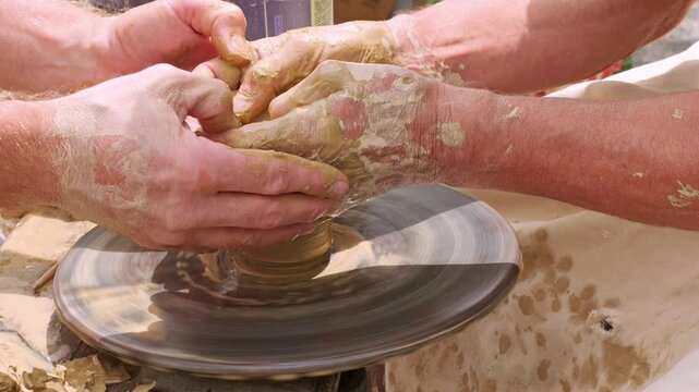 Potter and Student Shaping Clay on a Spinning Pottery Wheel With Hands Working Together