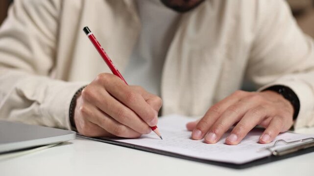Hand writes with red pencil on paper