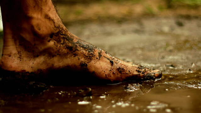 Close up of a dirty barefoot walking or standing in wet mud and puddle outdoors
