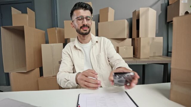 Man checks phone while seated at desk with laptop