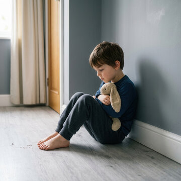 Sad Child Hugging Plush Toy In Corner Of Room