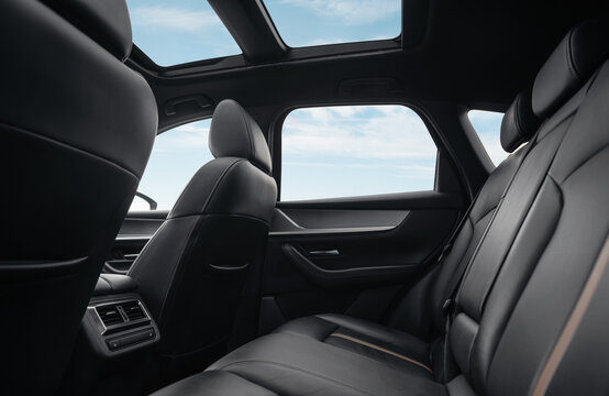 Rear row of seats in a car. SUV or wagon interior with black leather seats panoramic glass roof, blue sky with few clouds in the background.

