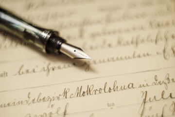 Eleganckie wieczne pióro leżące na starej rękopiśmiennej kaligrafii i pożółkłym papierze. Zabytkowy dokument historyczny, kaligrafia, literatura.