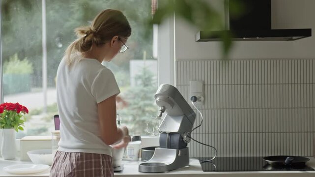 Woman attaching whisk to stand mixer in kitchen