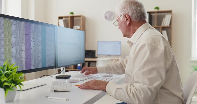 Senior man accountant working at computer in office. He reviews spreadsheet data on monitor, managing accounts and ensuring accuracy. Represents reliable professional expertise and productivity.