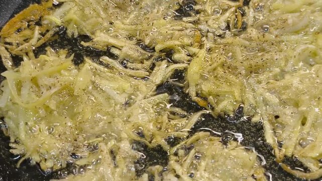 Large grated potato fritter cooking in a frying pan. Hot oil bubbles around the potato pancake as a golden crispy crust forms during frying. Homemade potato pancake made from coarsely grated potatoes.